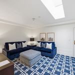 Bright living room with navy blue sectional sofa, geometric patterned rug, and skylight at el PRADO Hotel.