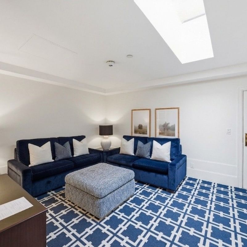 Bright living room with navy blue sectional sofa, geometric patterned rug, and skylight at el PRADO Hotel.