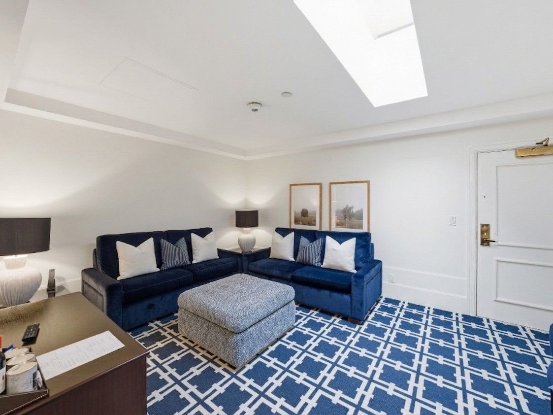 Bright living room with navy blue sectional sofa, geometric patterned rug, and skylight at el PRADO Hotel.