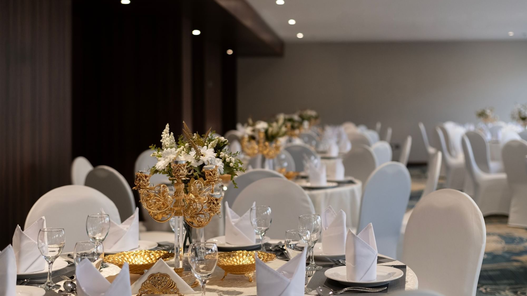 Banquet set-up with elegant place settings and a decorative gold centerpiece for a wedding in Warwick Hotels and Resorts