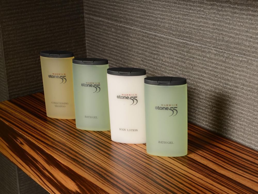Bottles of shampoo and lotion by a grey wall on a wood-grain shelf in Executive Room at Warwick Stone 55 - Beirut