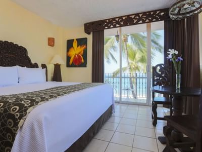 Hotel room with carved wood bed, ocean view balcony, and tropical palm trees at Playa Los Arcos Puerto Vallarta 2023