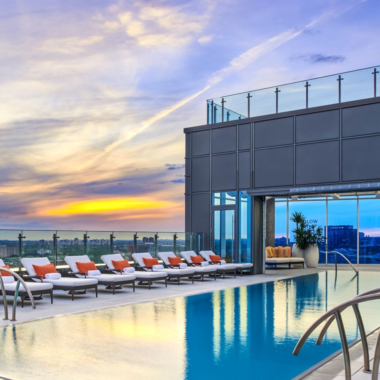 Rooftop swimming pool facing sunset sky with sun loungers beside glass modern building wall at Hotel X Toronto
