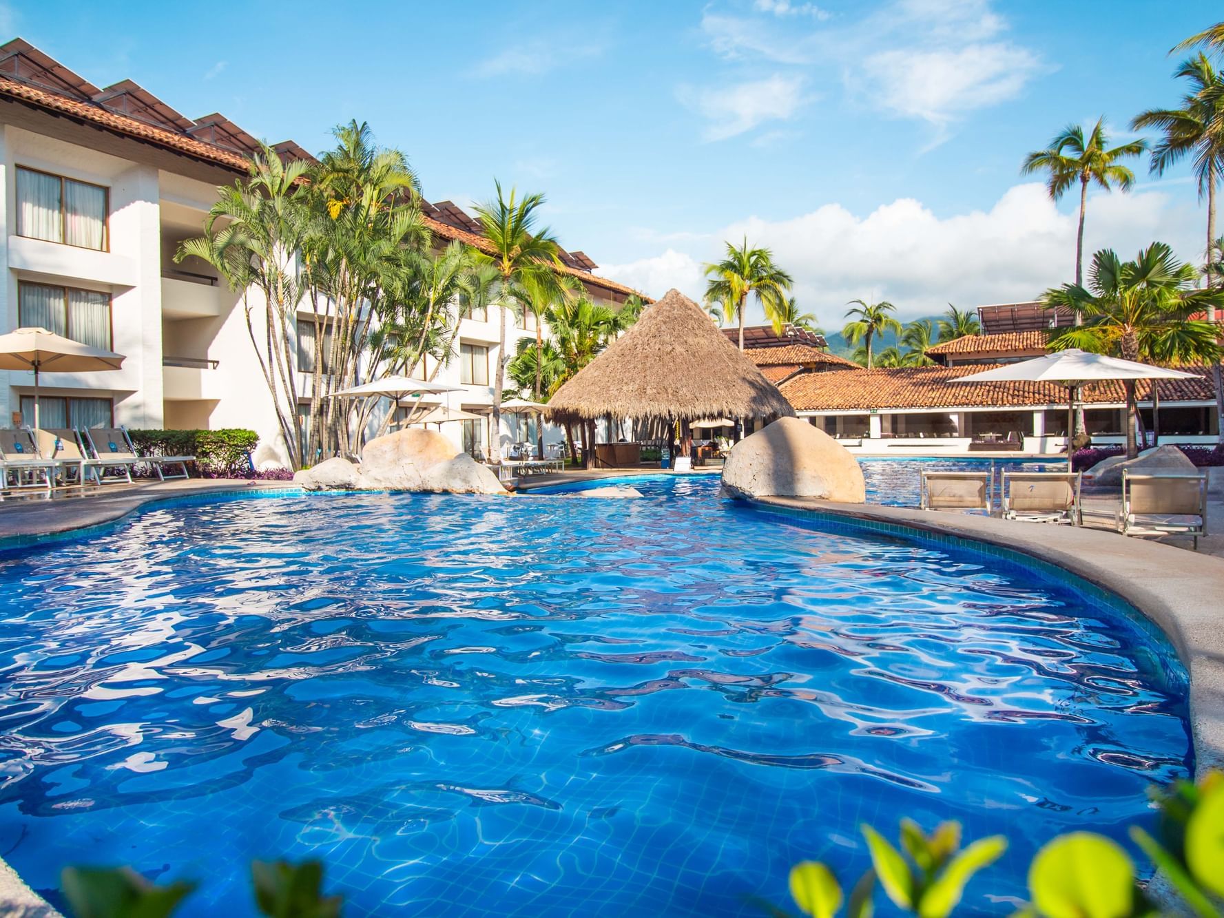 Piscina con gran palapa rodeada de palmeras en Guadalajara Plaza Hoteles & Suites