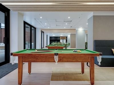 Modern recreation room with pool tables, lounge seating, and kitchen area at UniLodge Auckland Central.
