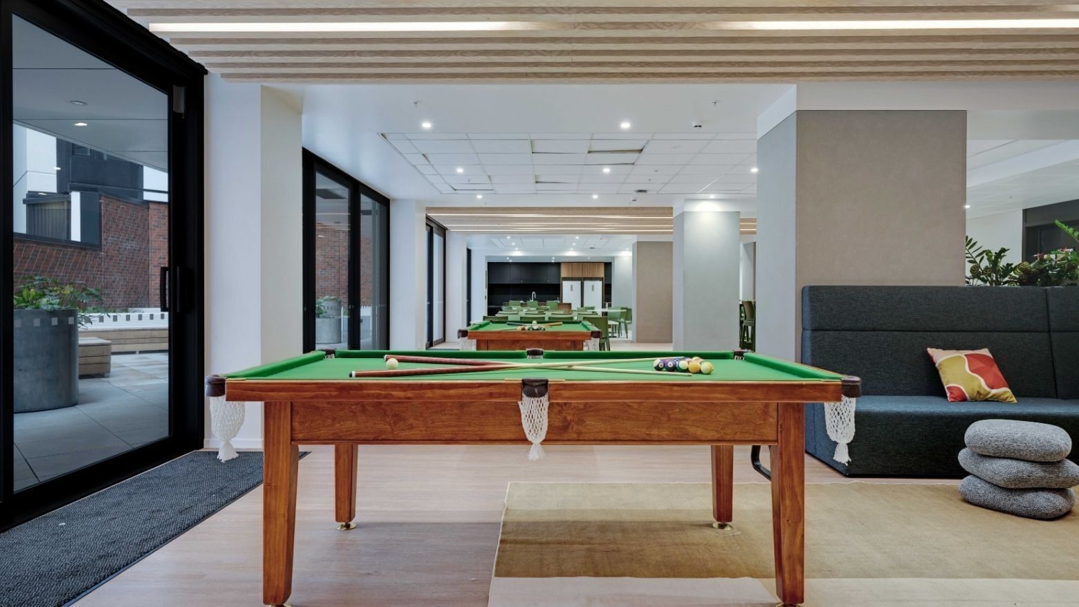 Modern recreation room with pool tables, lounge seating, and kitchen area at UniLodge Auckland Central.