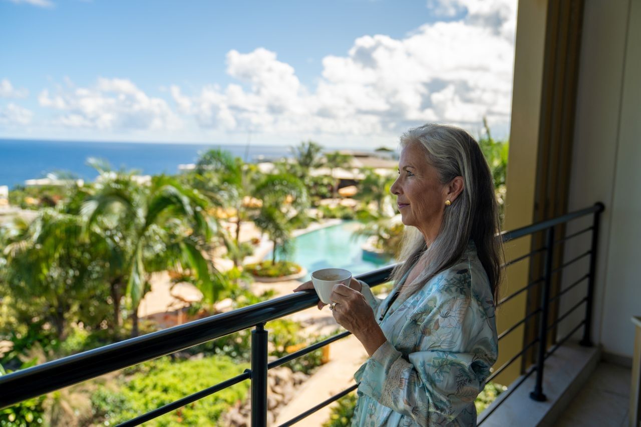 Person enjoying a coffee on the balcony while gazing at an ocean view in Deluxe Ocean View Room at Golden Rock Resort
