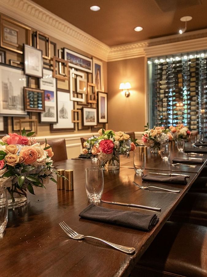 Private Dining features a long wood table by flowers under a gallery wall at Warwick Melrose Dallas