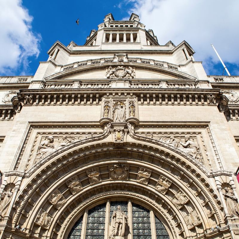Ornate building with large arched entrance and detailed sculptures under a blue sky with white clouds.