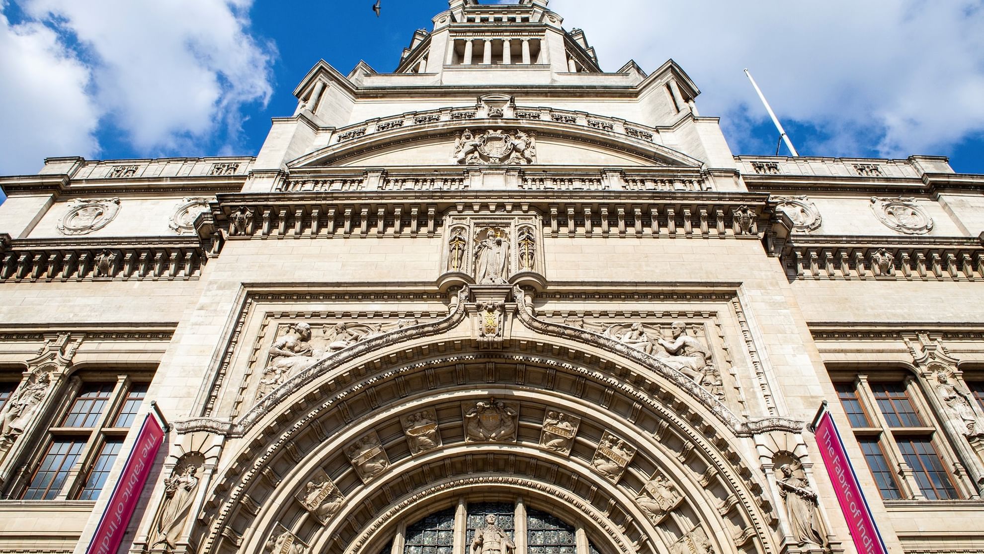 Ornate building with large arched entrance and detailed sculptures under a blue sky with white clouds.
