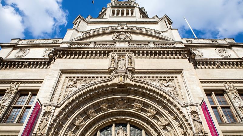Ornate building with large arched entrance and detailed sculptures under a blue sky with white clouds.