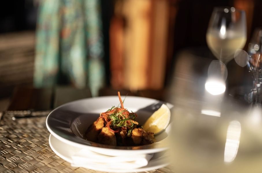 Gourmet dish with a lemon wedge by a wine glass in Wicked Walu at Warwick Fiji Resort and Spa