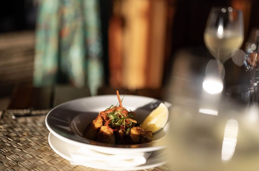 Gourmet dish with a lemon wedge by a wine glass in Wicked Walu at Warwick Fiji Resort and Spa