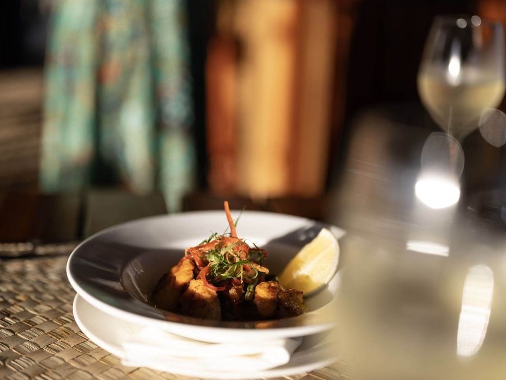 Gourmet dish with a lemon wedge by a wine glass in Wicked Walu at Warwick Fiji Resort and Spa