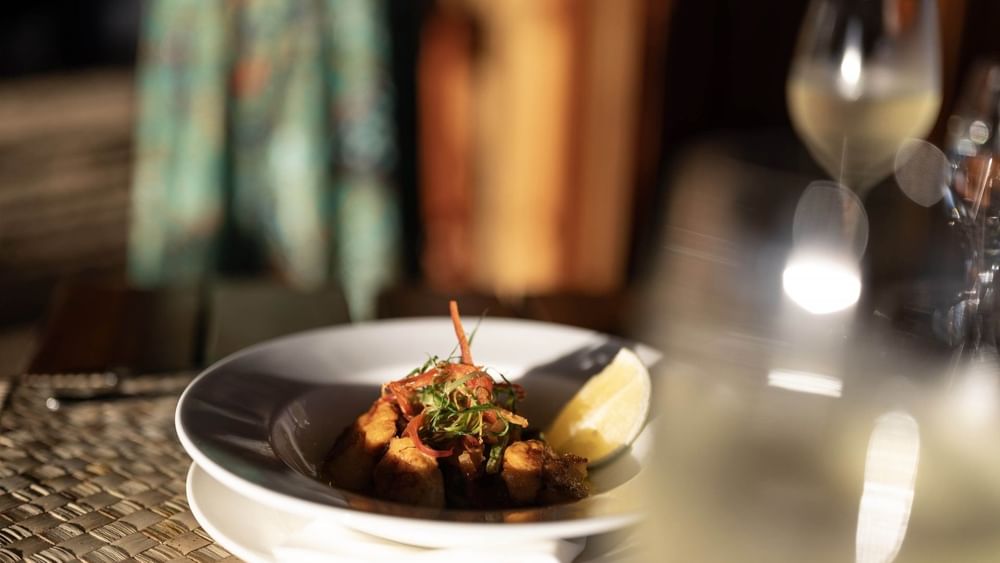 Gourmet dish with a lemon wedge by a wine glass in Wicked Walu at Warwick Fiji Resort and Spa