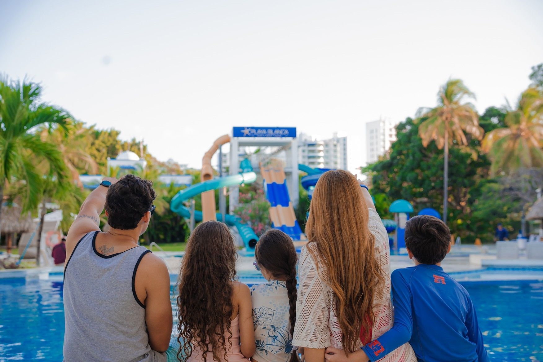 Family of five viewing colorful water slides and pool area surrounded by palm trees at Playa Blanca Beach Resort