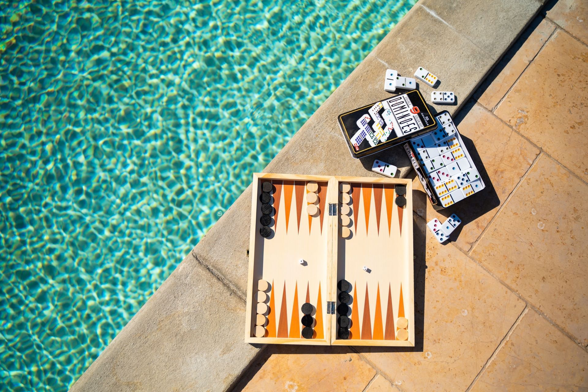 Backgammon set and scattered dominoes on a stone edge by a shimmering pool at Golden Rock Resort
