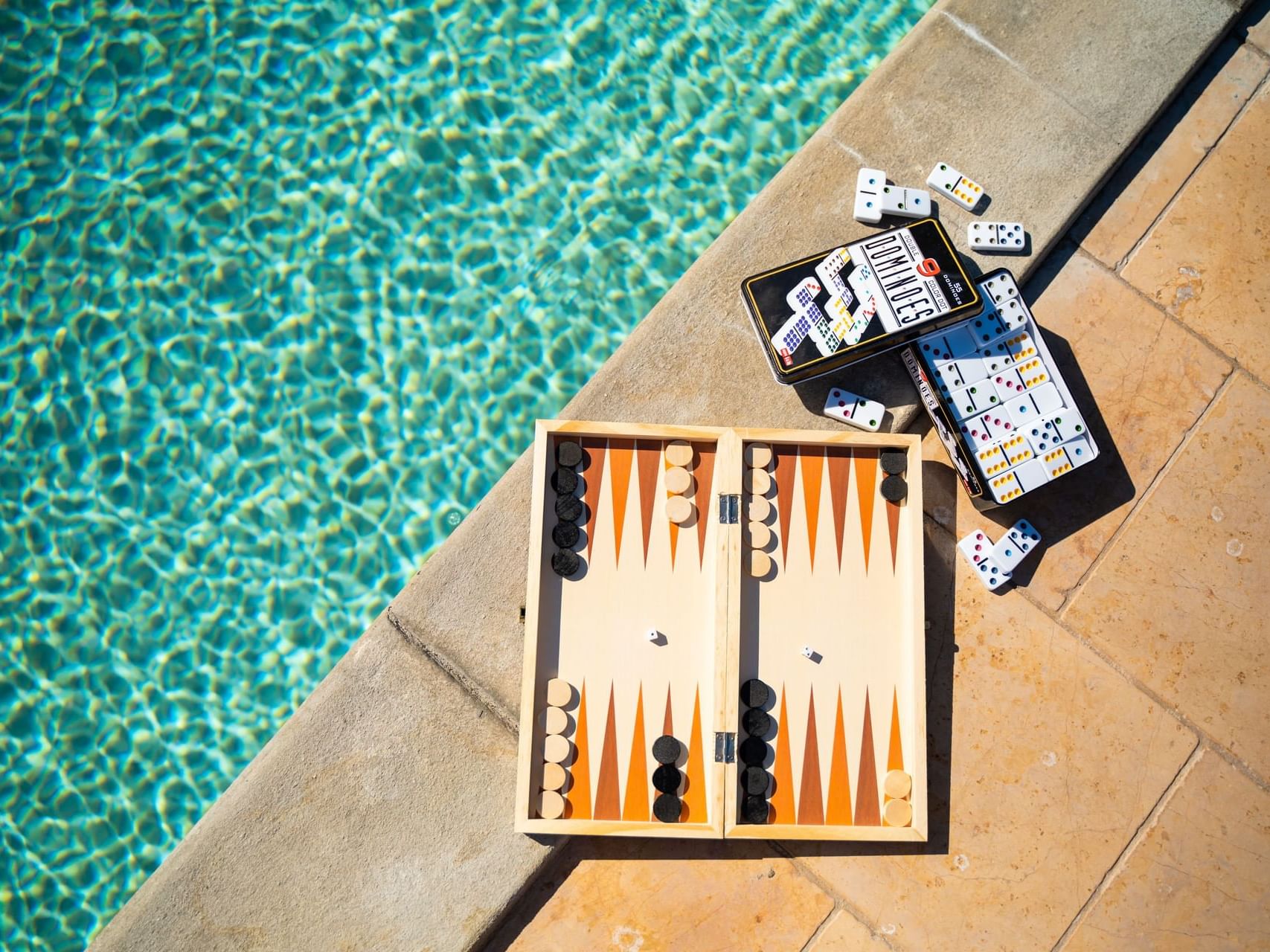 Backgammon set and scattered dominoes on a stone edge by a shimmering pool at Golden Rock Resort