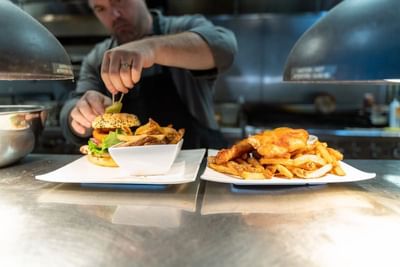 A chef garnishing a burger dish at Hotel Clique Calgary Airport