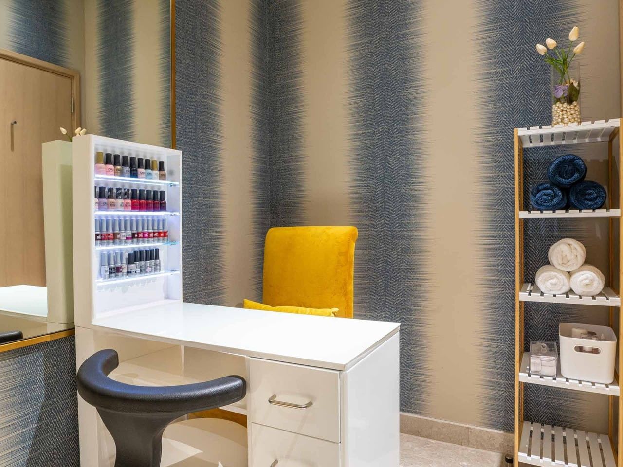 White desk with drawers, yellow chair, and blue-striped wall in a room with a mirror and shelf.