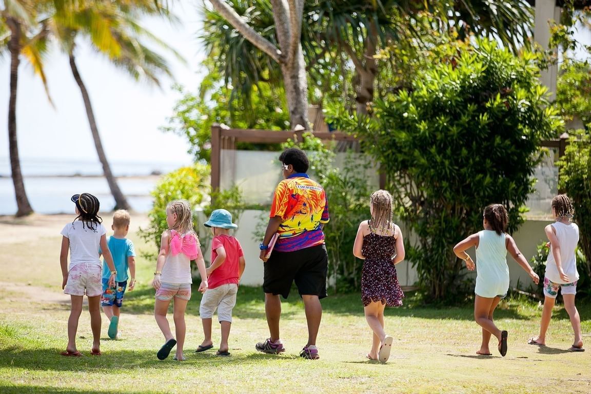 Children walking by green bushes near a beach under the care of a supervisor at The Naviti Resort - Fiji