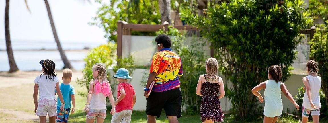 Children walking with an adult by the beach at The Naviti Resort in Korolevu