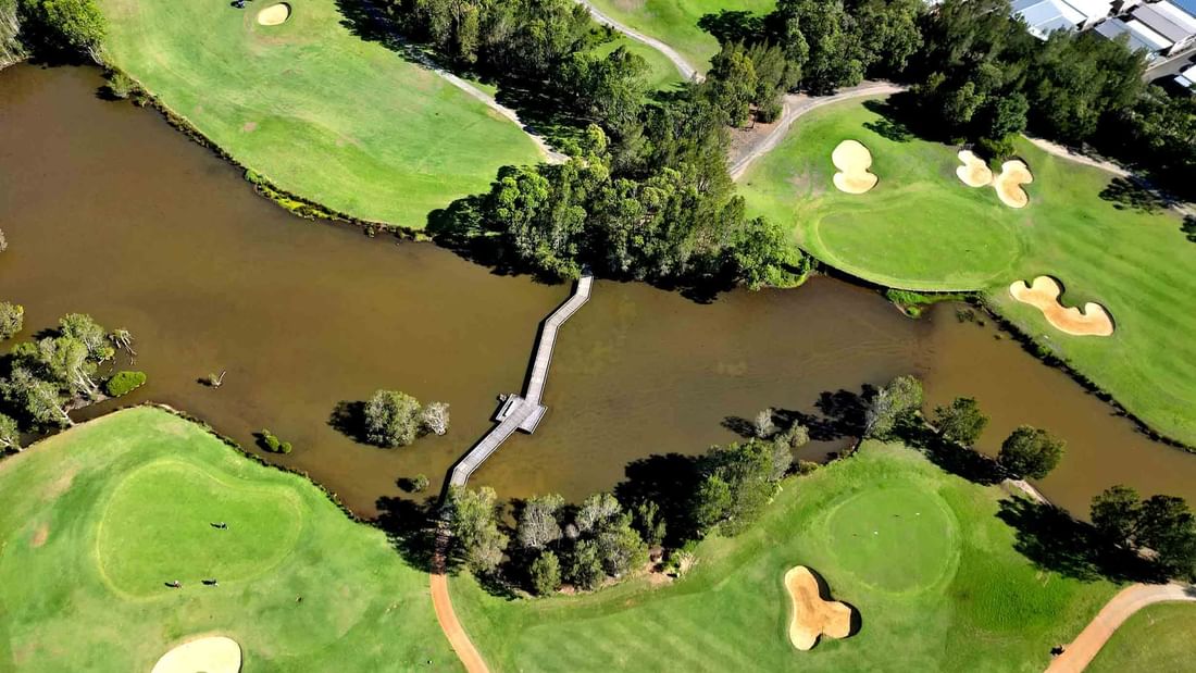 Aerial view of a golf course with ponds, sand bunkers, and a footbridge near Mercure Kooindah Waters