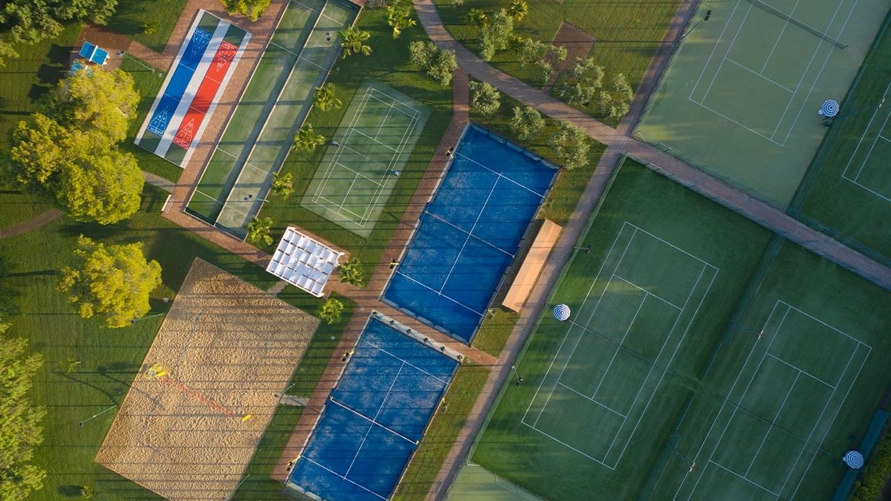 Aerial view of a resort with tennis courts, a swimming pool, and a beach volleyball area.