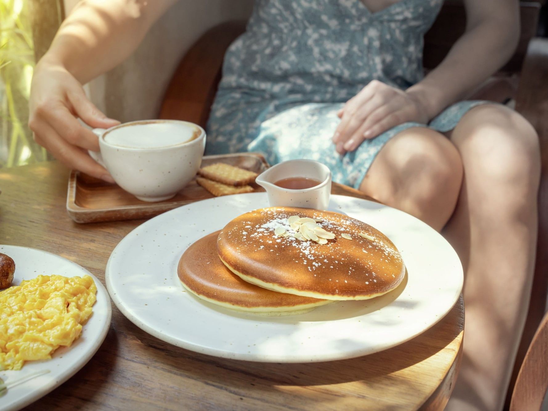 A woman enjoys a breakfast spread featuring fluffy pancakes, scrambled eggs, sausage, toast, and coffee at a cozy diner.