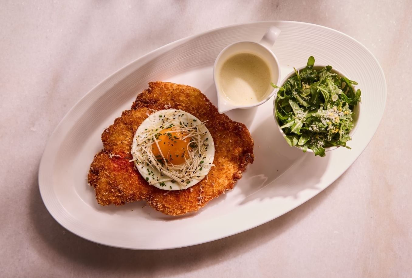 Plat de poulet pané accompagné d'un œuf et d'une salade, servi dans une assiette blanche, tiré du menu du restaurant Whitcomb's situé à l'intérieur de l'hôtel The Londoner