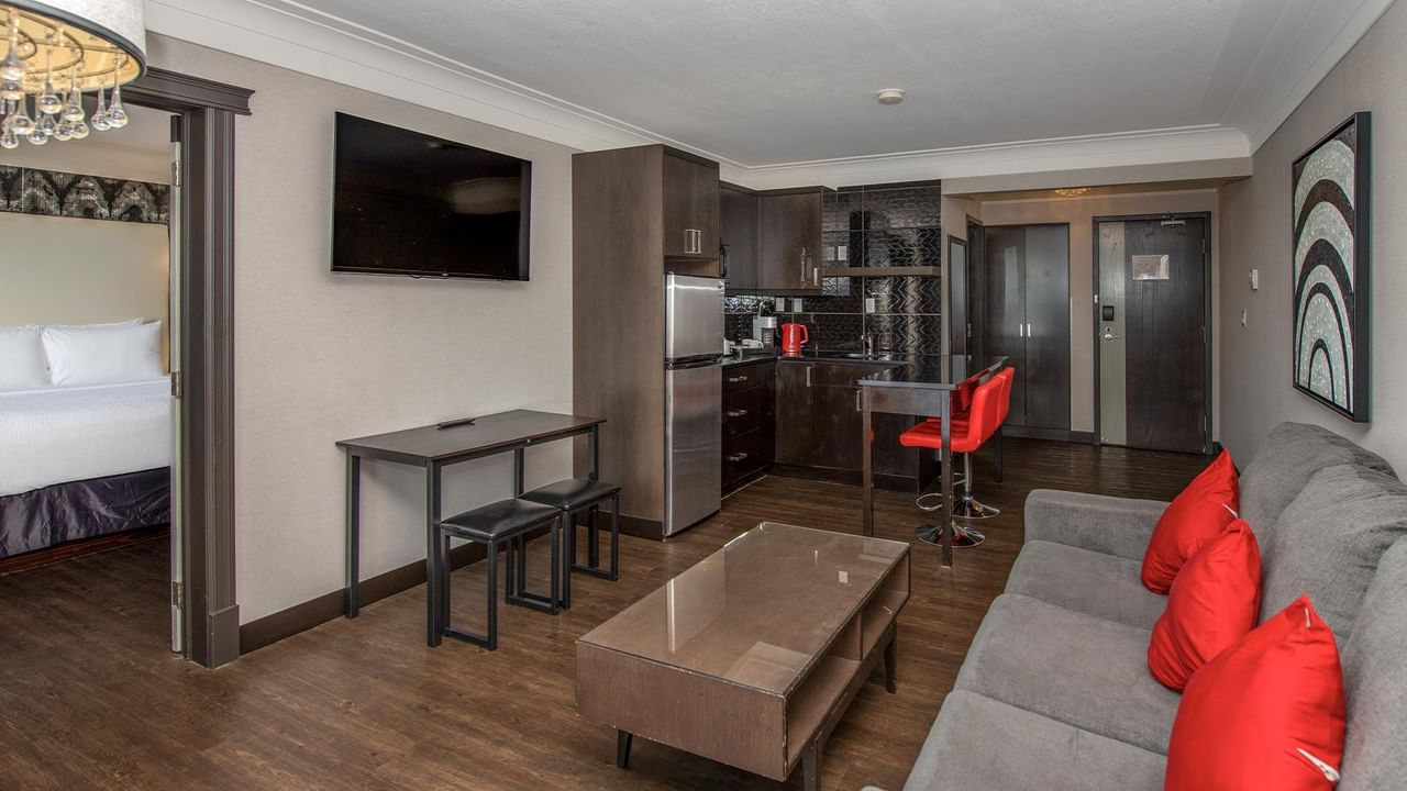 Modern suite with kitchenette, gray sofa with red pillows, and dining area at Coast Calgary University Area Hotel by APA.