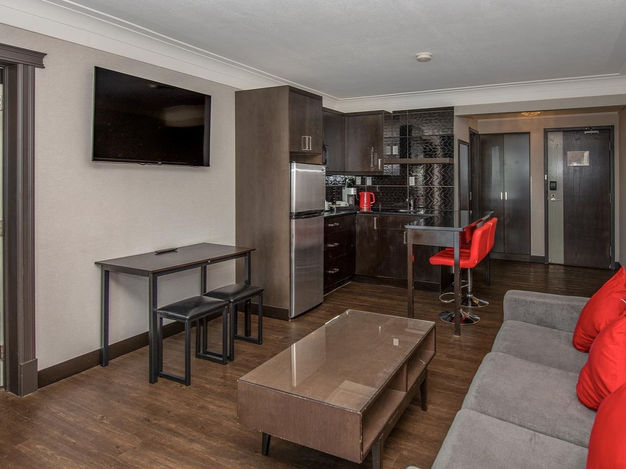 Modern suite with kitchenette, gray sofa with red pillows, and dining area at Coast Calgary University Area Hotel by APA.