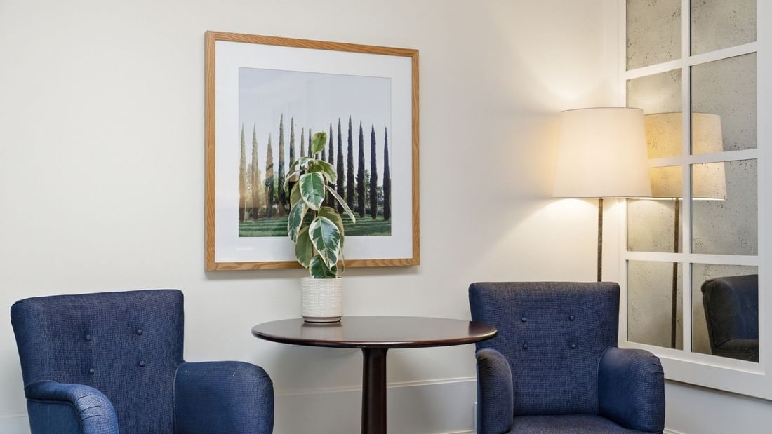 Grand Deluxe Suite seating area with two blue armchairs, round table, and framed artwork at el PRADO Hotel
