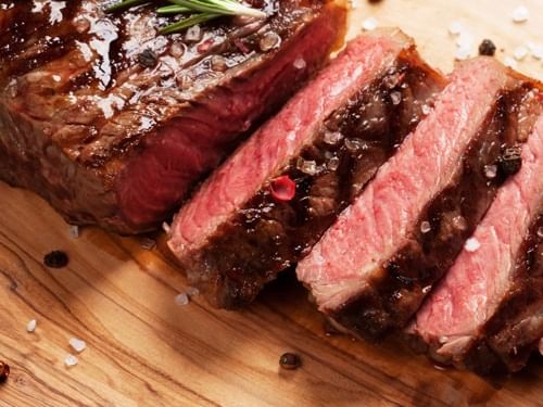 Sliced steak on a wooden cutting board with rosemary, salt, and pepper.