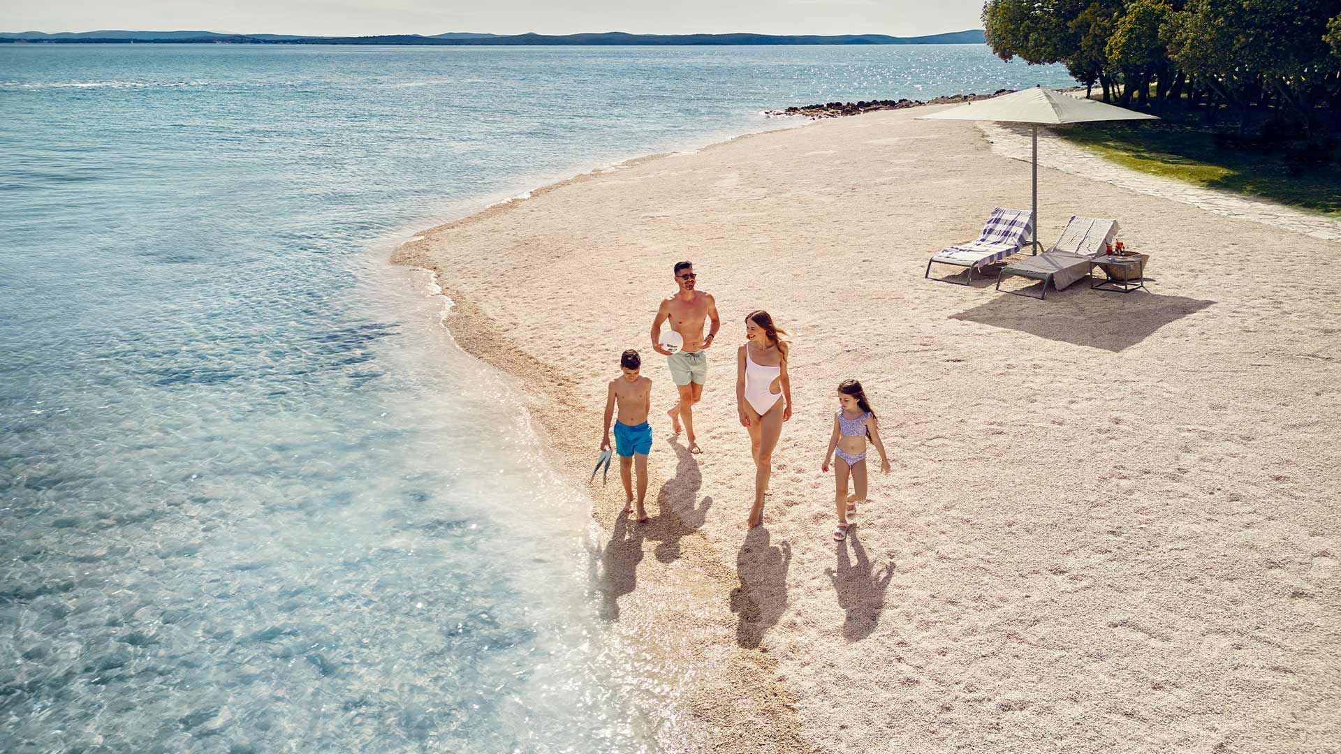 Obitelj uživa u privatnoj plaži s ležaljkama i suncobranom na čistom moru.