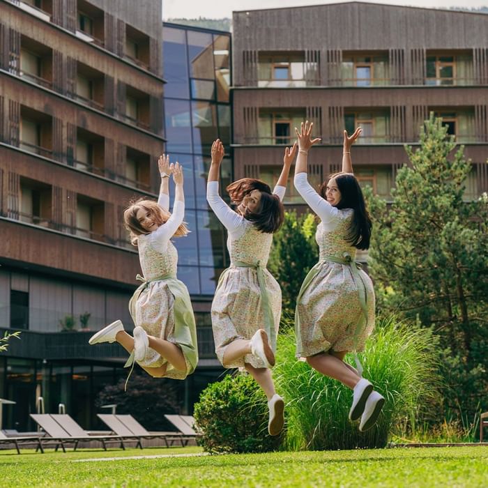 Drei Frauen in Schürzen springen vor einem modernen Gebäude in die Luft.