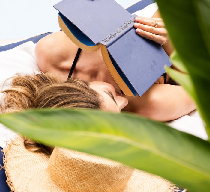 Relaxing poolside scene near Riviera Hotel South Beach featuring a woman napping with a book over her face and a sun hat