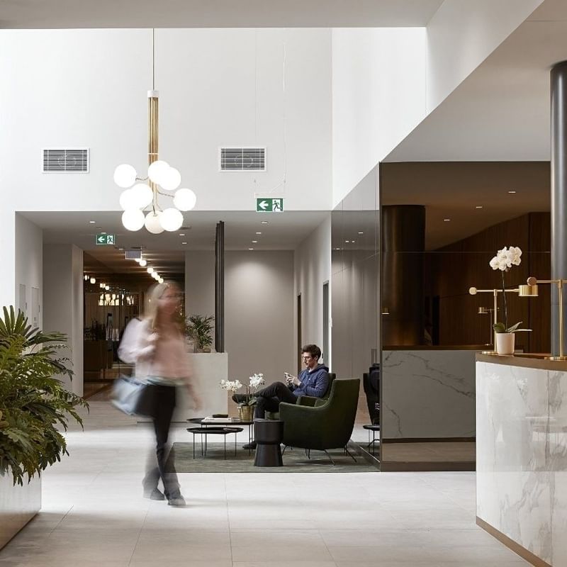 Woman walking in a BTR lobby with a man seated in green chair and another woman at the front desk.