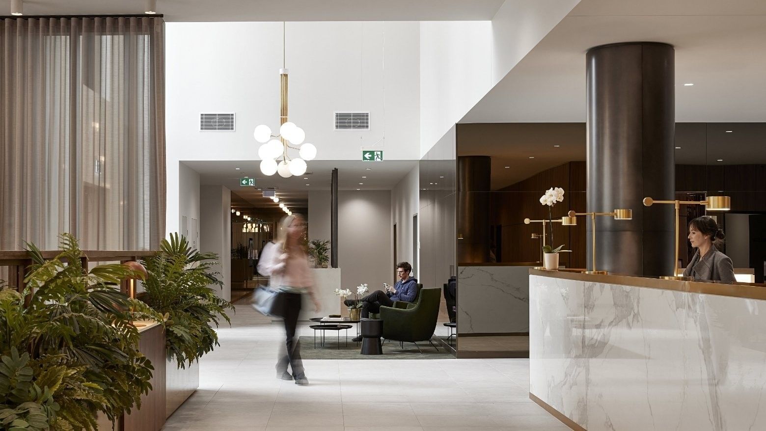 Woman walking in a BTR lobby with a man seated in green chair and another woman at the front desk.