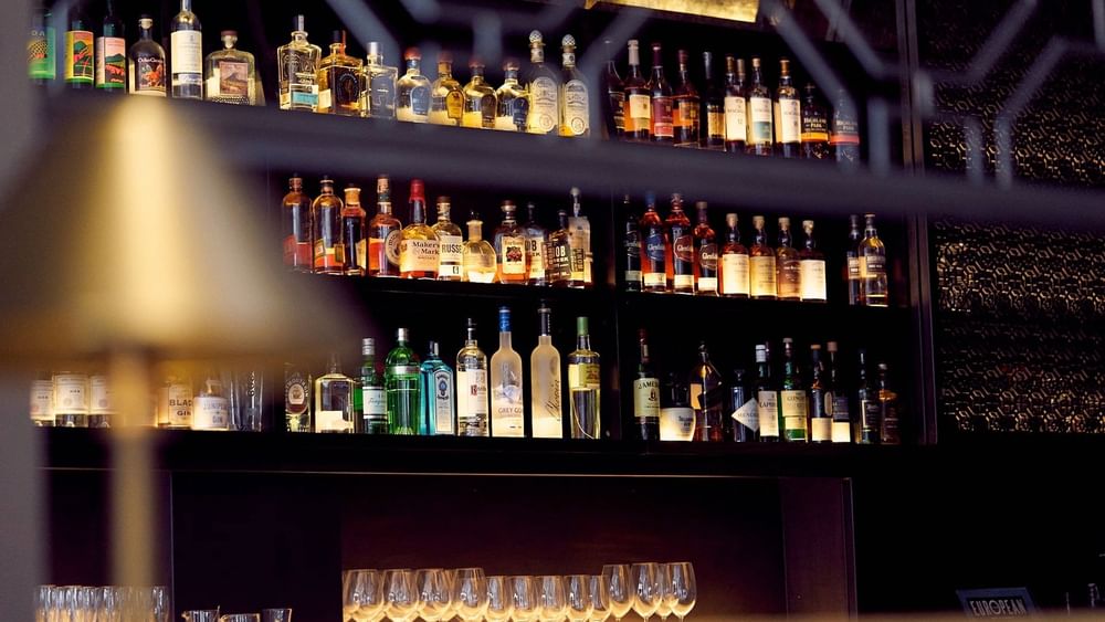 The European features Liquor bottles on backlit shelves by rows of wine glasses at Warwick San Francisco