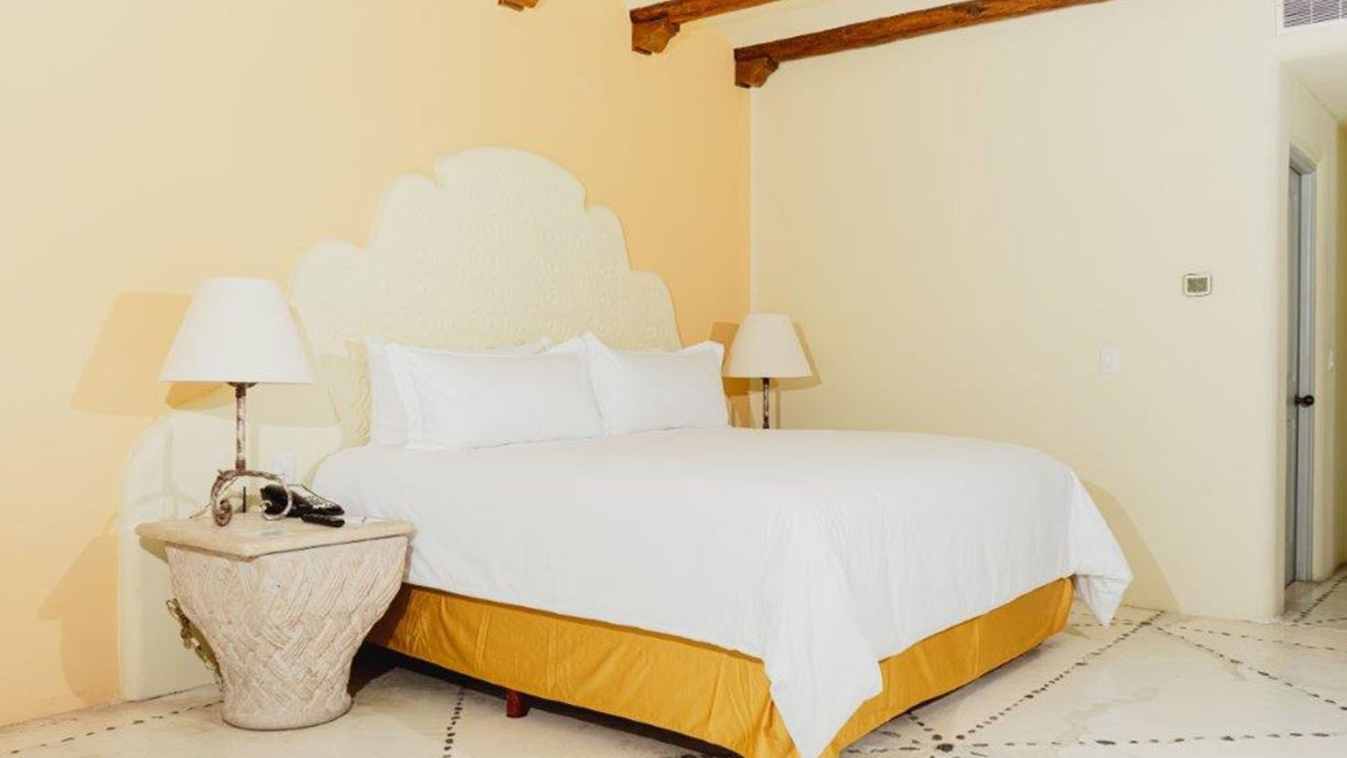 King Master Suite featuring a king bed, ornate white headboard, and warm yellow lighting at Quinta Real Huatulco