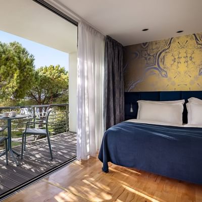 Hotelzimmer mit Balkon, Tisch, Stühlen und Meerblick durch große Glastüren.