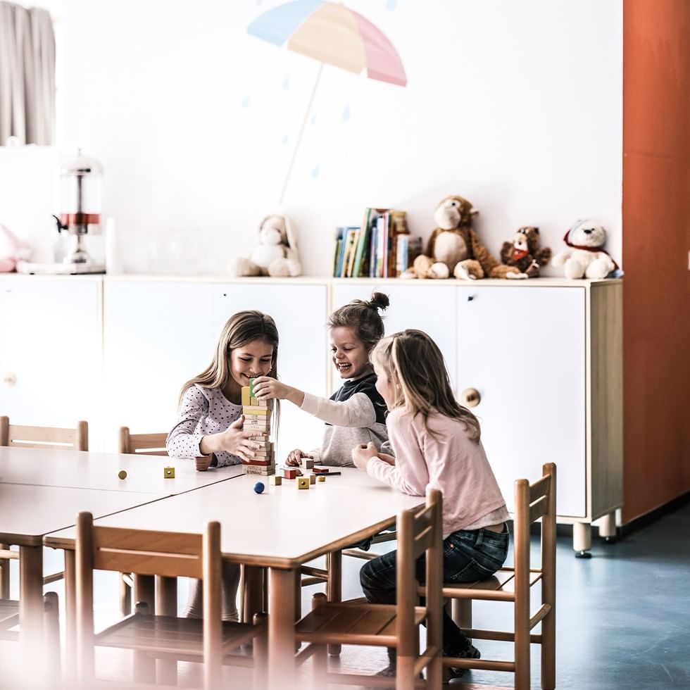 Drei Kinder spielen mit Bauklötzen am Tisch im Kinderzimmer bei Falkensteiner Hotel Cristallo