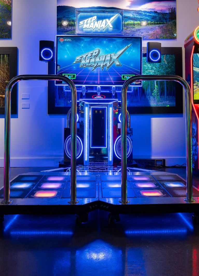 Step Maniax dance platform with glowing panels, under a screen and speakers with metal rails at Hotel X Toronto