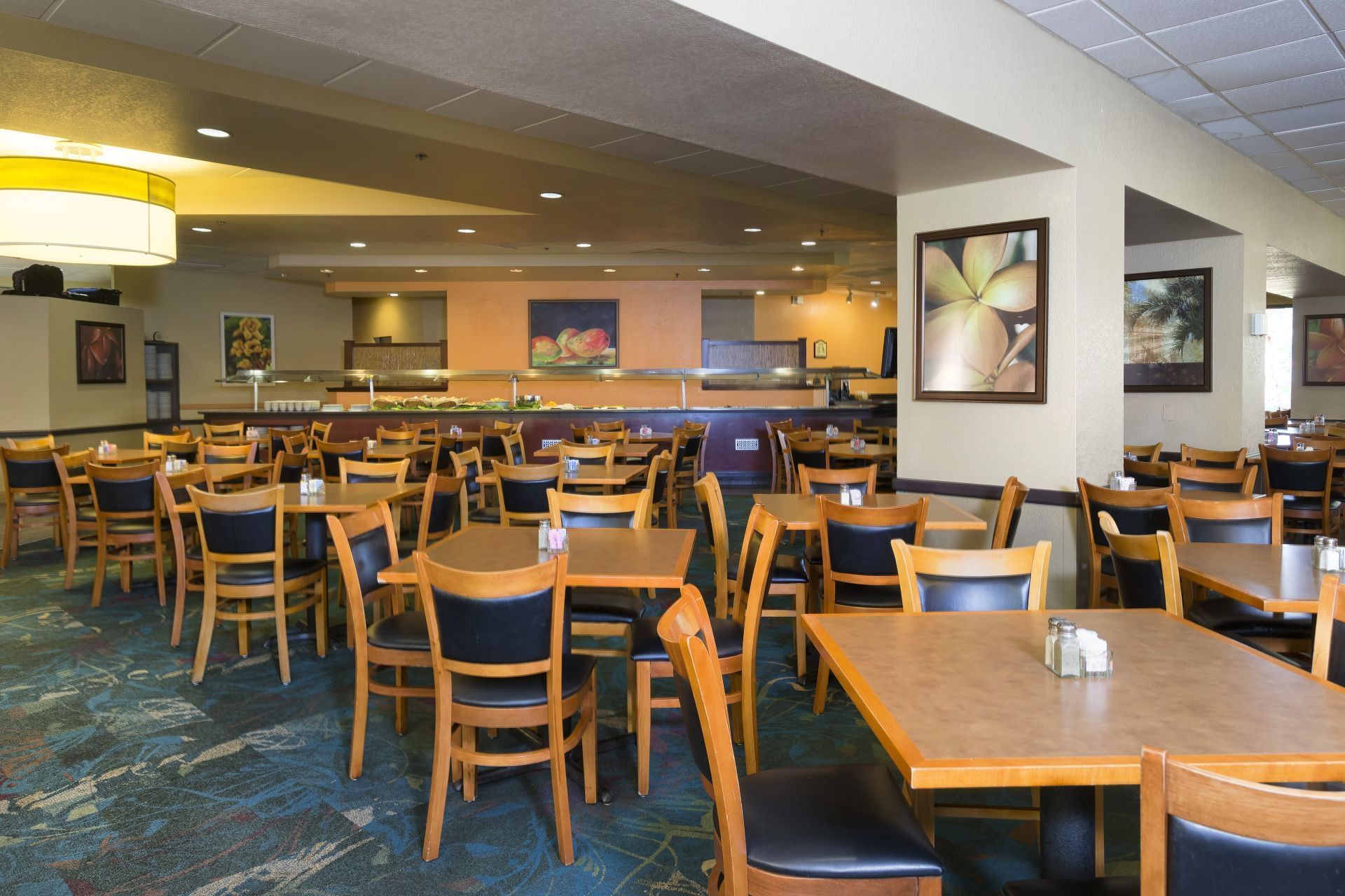 A large dining room with tables and chairs, a buffet in the background, and artwork on the walls.