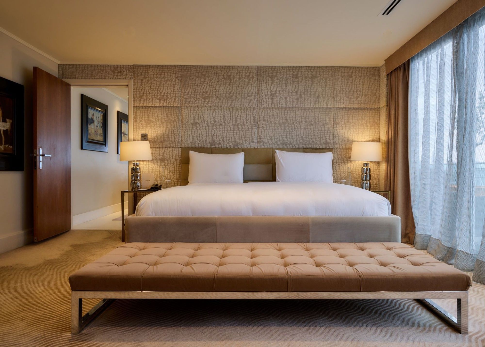 Spacious Penthouse Suite with king bed, tufted bench, textured wall panels, and bedside lamps at The May Fair Hotel, London.