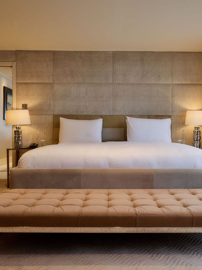 Spacious Penthouse Suite with king bed, tufted bench, textured wall panels, and bedside lamps at The May Fair Hotel, London.