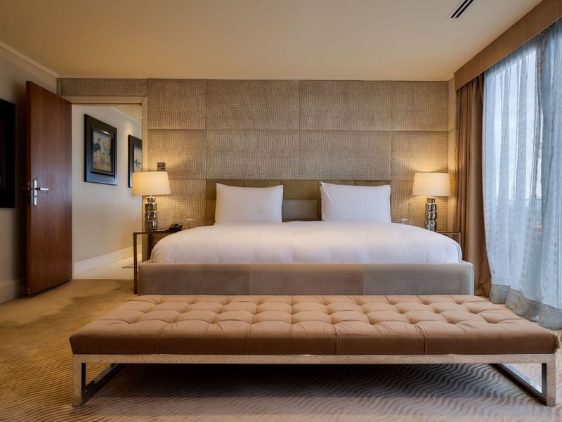 Spacious Penthouse Suite with king bed, tufted bench, textured wall panels, and bedside lamps at The May Fair Hotel, London.