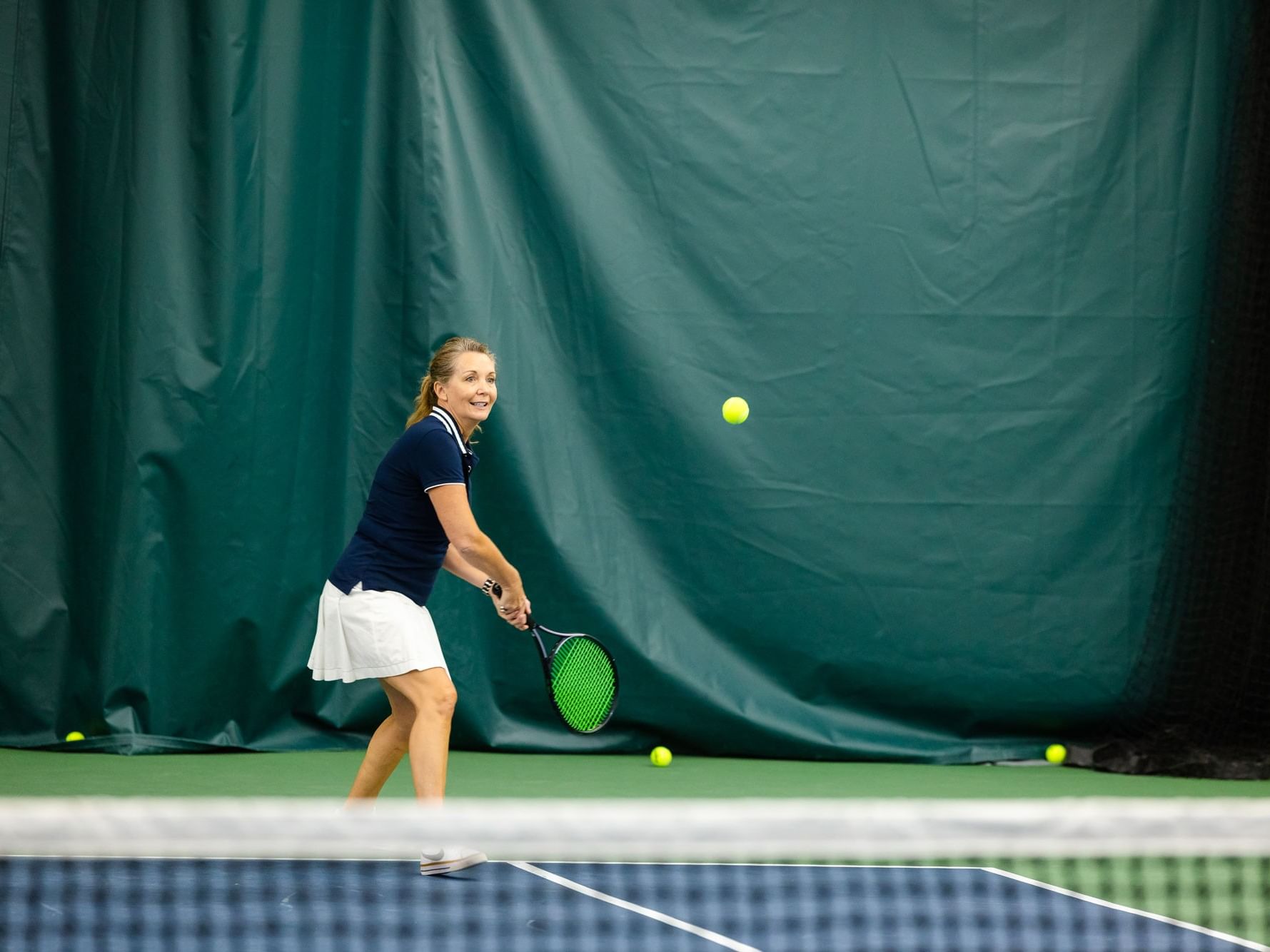 Woman hitting a tennis ball with a racket in a court for the 3.0+ Tennis Groundstrokes Clinic.