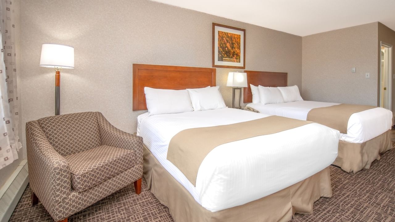 Two beds, a chair, and a lamp in a hotel room.